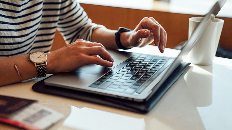 Une personne utilisant un ordinateur portable à un bureau, les mains posées sur le clavier et le pavé tactile