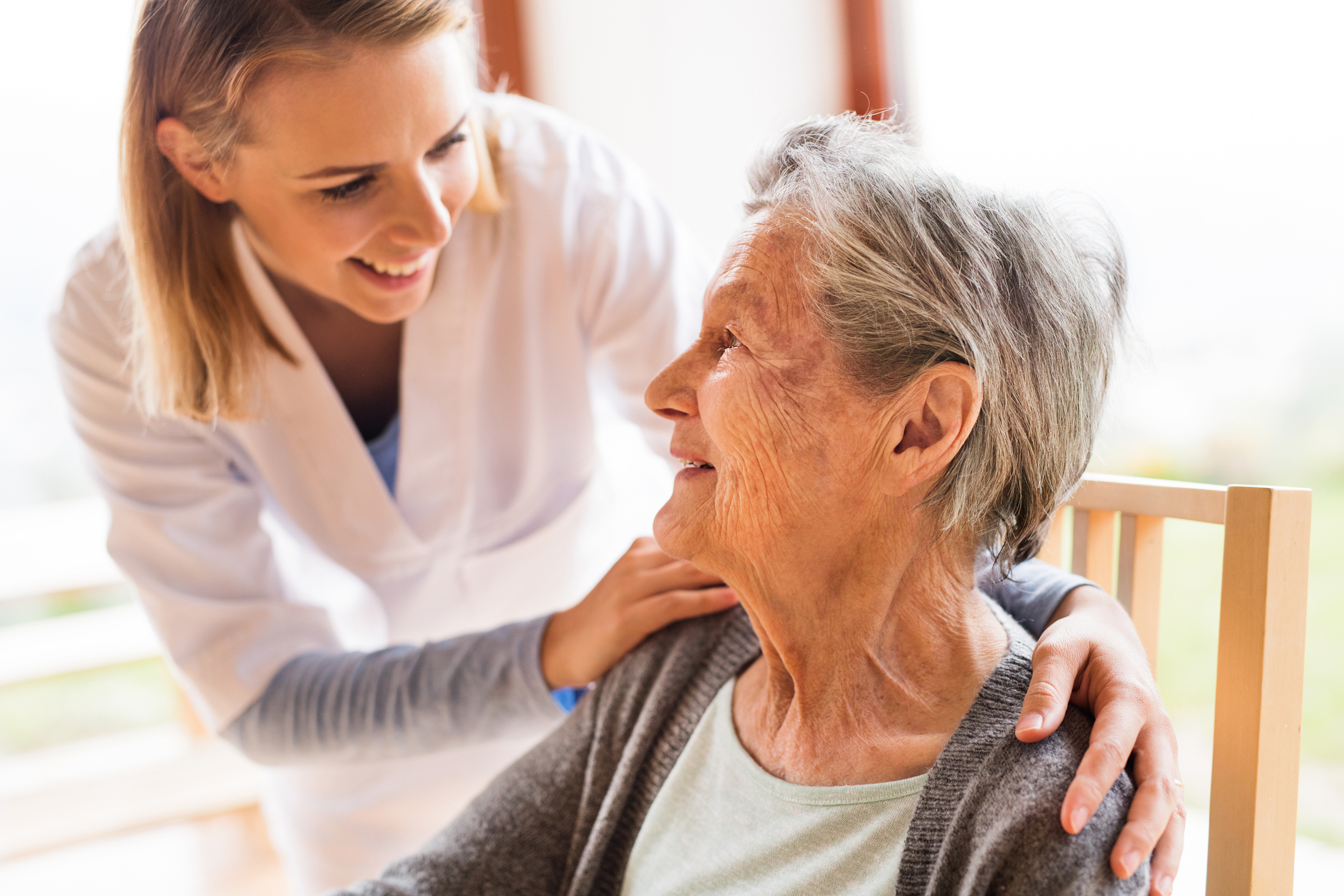 Young female worker touches shoulder of elderly woman in wheelchair