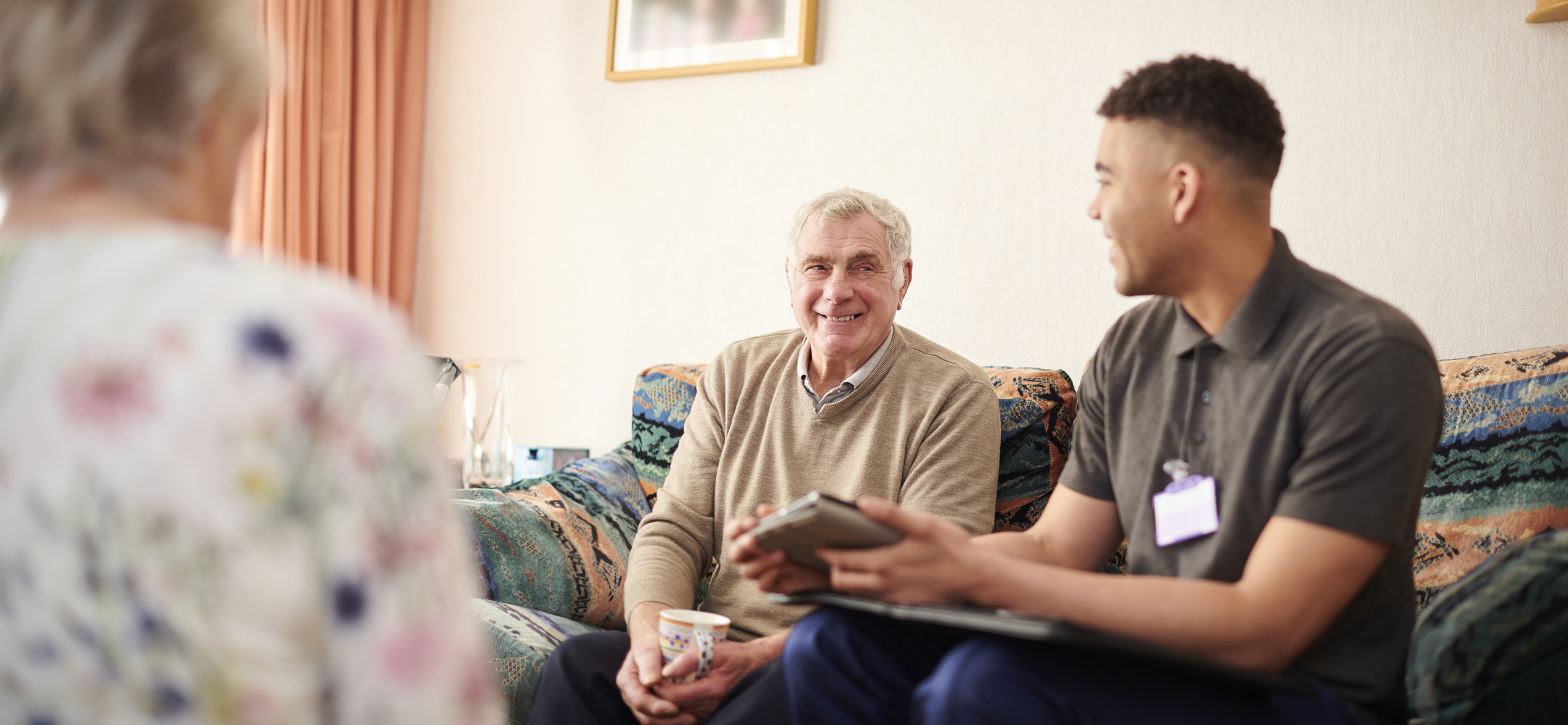 A young man sits in the living room with an older man and woman. 
